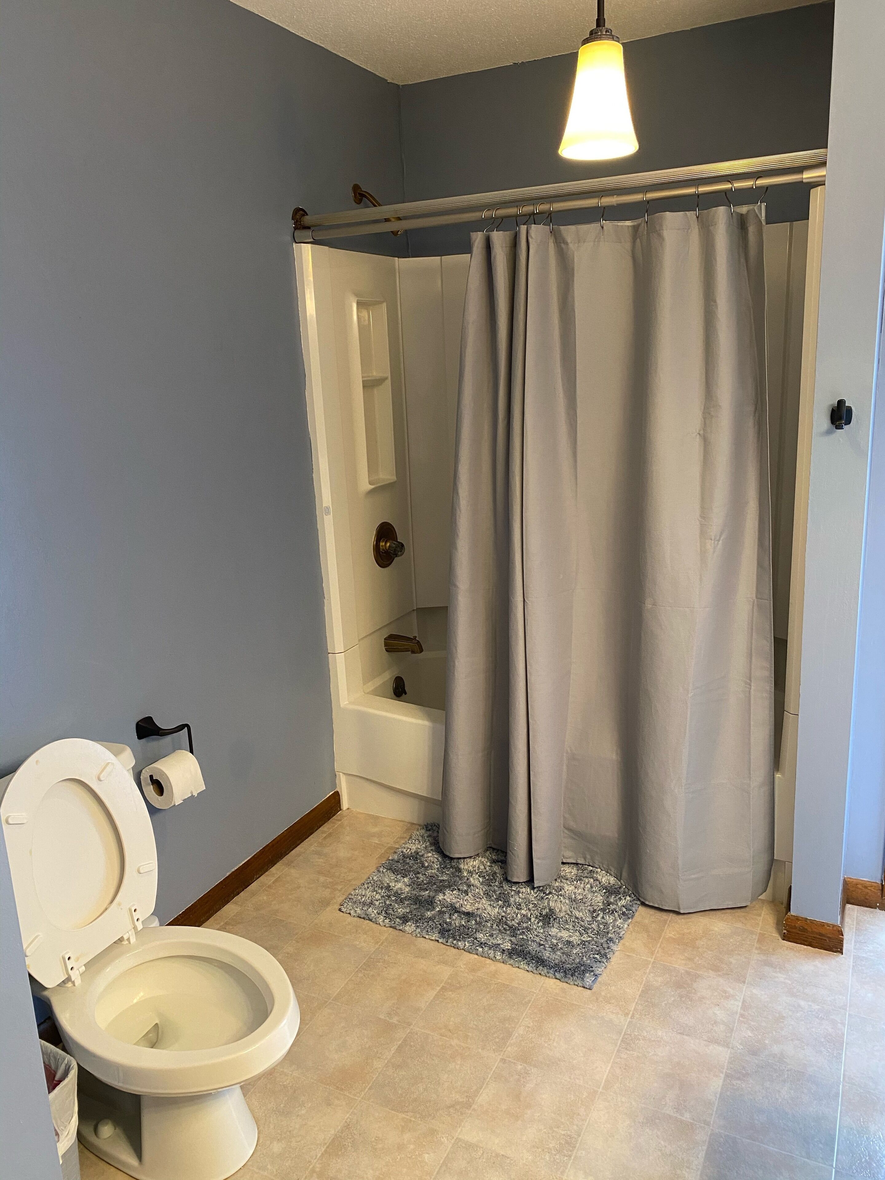 A bathroom with a toilet, a shower curtain, a bathtub, and a towel rack.