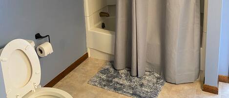 A bathroom with a toilet, a shower curtain, a bathtub, and a towel rack.