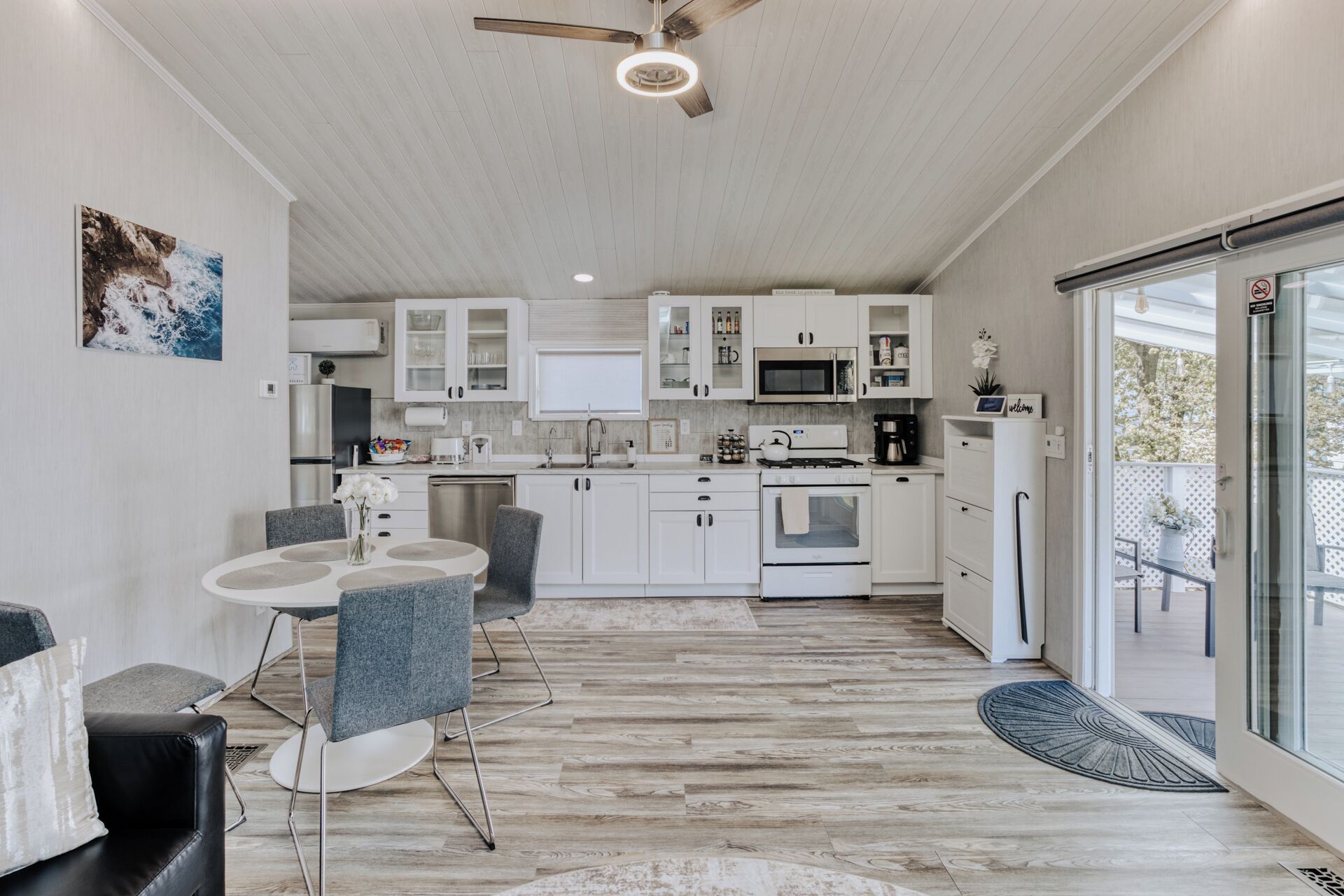 A modern kitchen with white cabinets, a dining area with grey chairs, and a large window.
