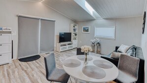Un salon moderne avec un ventilateur de plafond, un téléviseur, une table ronde avec des chaises, un canapé et une bibliothèque.