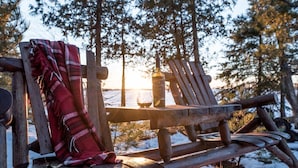 A wooden bench with a blanket and a bottle, set against a snowy forest backdrop.