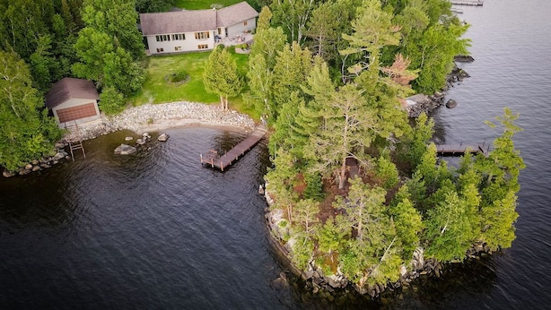 An aerial view of a lakeside property with a main house, a dock, and a small boat.