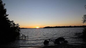 A sunset over a calm body of water with a dock and rocks in the foreground.