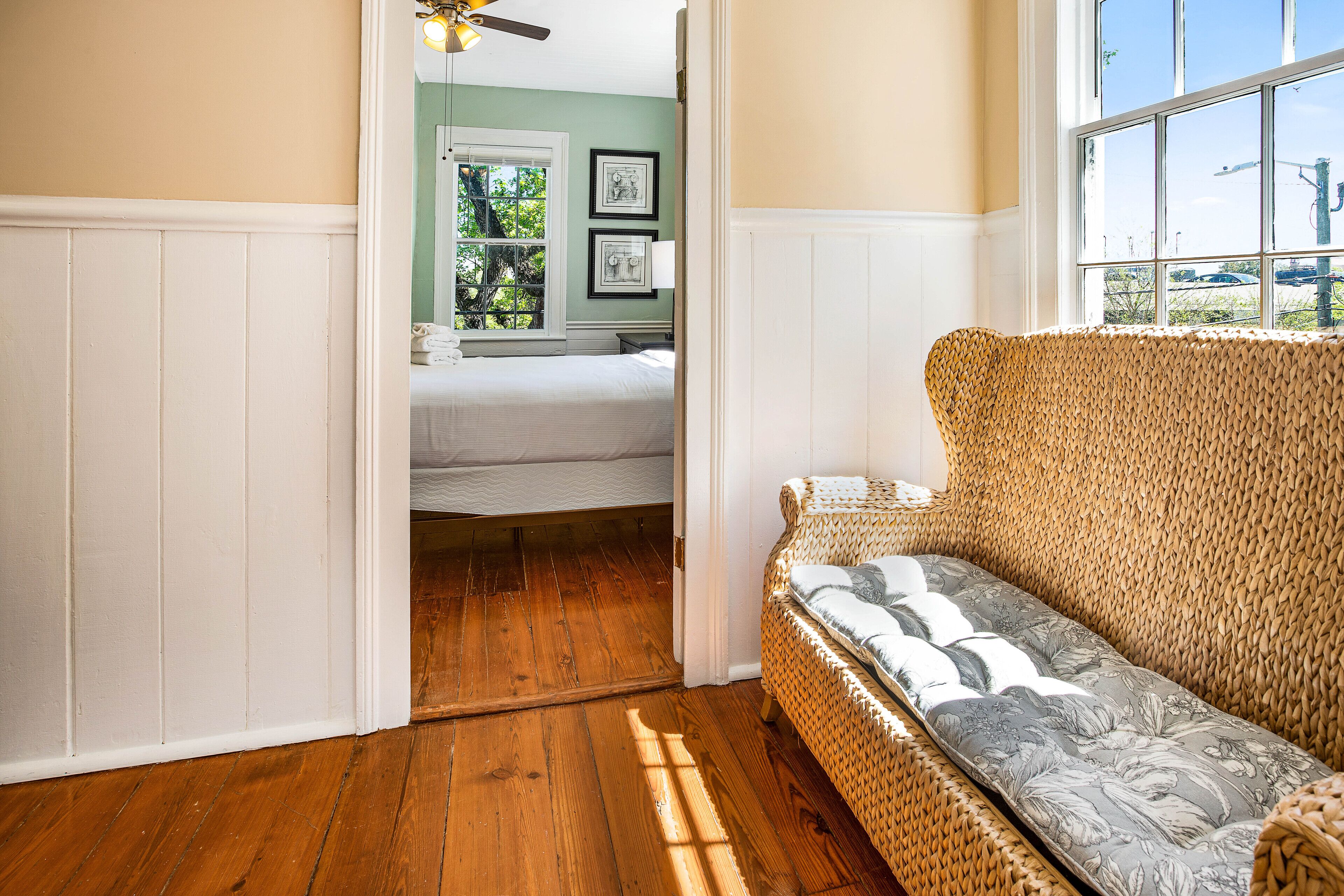 Una habitación con sofá de mimbre, suelo de madera y cama con cabecera blanca.
