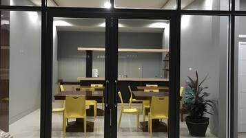 A modern interior with a dining area featuring a long table and yellow chairs, a potted plant, and a glass partition.