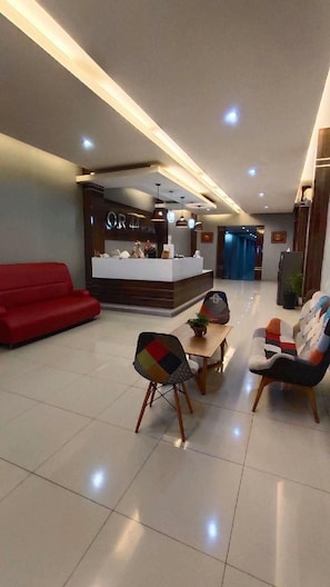 A hotel lobby with a reception desk, a red sofa, and a dining area with chairs and a table. - O R 44 Hotel Bengkulu (Bengkulu)