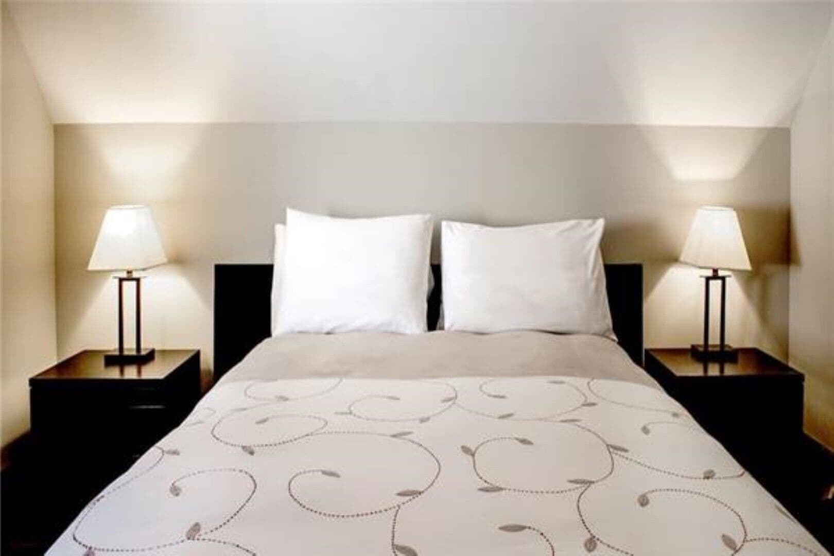 A hotel room with a bed, two bedside tables, and two lamps.