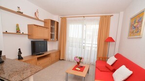 Ein Wohnzimmer mit Fernseher, Holzschränken, einem roten Sofa und einem Couchtisch mit Blumen in einer Vase.