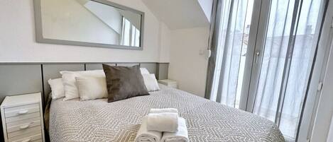 A bedroom with a large bed, a nightstand, a mirror, and a window with curtains.