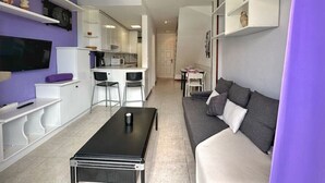 A compact living space with a sofa, a coffee table, a TV, and a kitchenette. - Apartamento con piscina junto a la playa - La Aren (Arnuero)