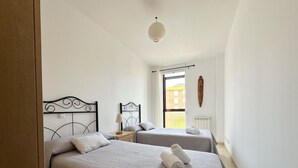 Un dormitorio con dos camas, una ventana, un radiador y una lámpara colgante.