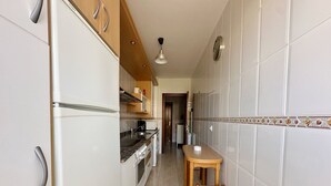 Una cocina estrecha con armarios blancos, una mesa de madera y una silla.