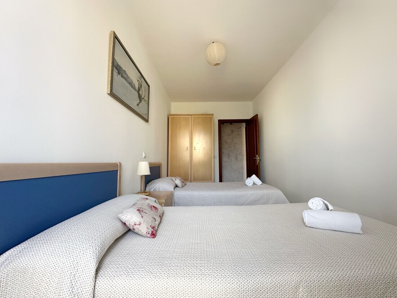Habitación de hotel con dos camas, un armario, una puerta y un cuadro en la pared.