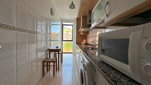 Una cocina con microondas integrado, un lavabo y una lavadora. Hay un comedor con mesa y sillas.