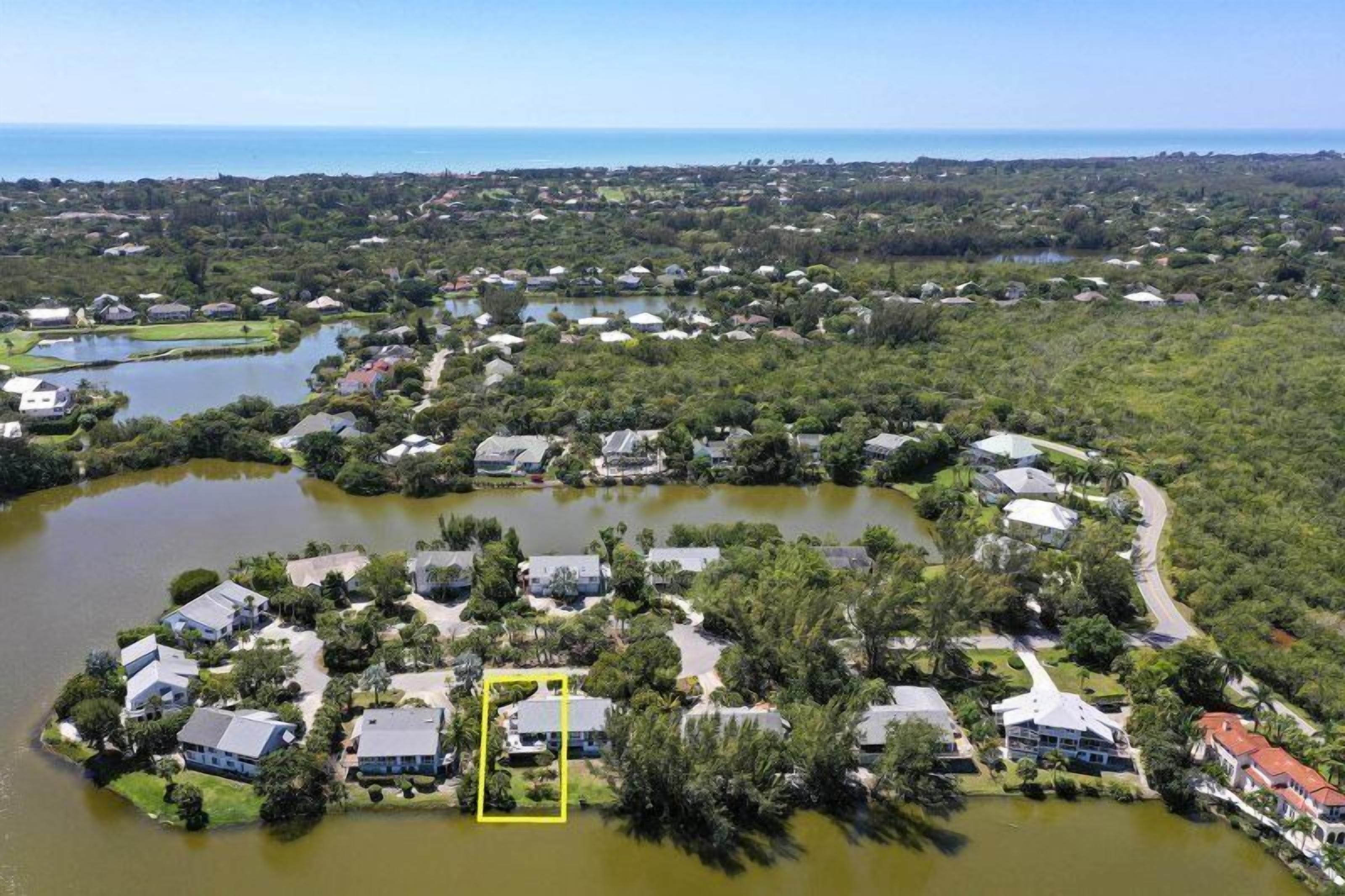 An aerial view of a residential area with houses, a lake, and a clear view of the ocean.