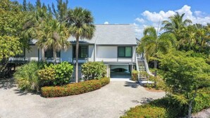 A modern two-story house with a covered porch, surrounded by lush greenery and palm trees. - A Peace of Heaven (Sanibel)