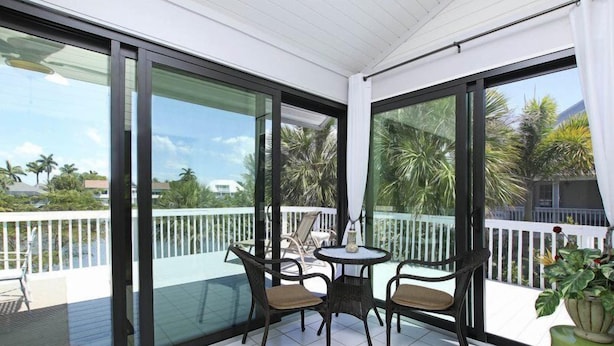 A balcony with glass doors, a small table, two chairs, and a potted plant. - A Peace of Heaven (Sanibel)
