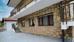 A two-story house with stone facade, a balcony, and a concrete driveway.