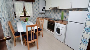A compact kitchen with a dining table, chairs, a washing machine, a stove, and a refrigerator.
