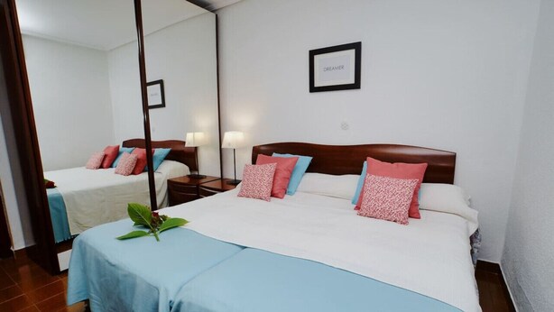 A hotel room with a large bed, a bedside table, a lamp, and a mirror.