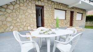 A stone building with a white table and chairs, a door, and a window with shutters.