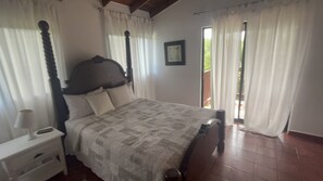 Ein Schlafzimmer mit einem Bett, einem Nachttisch, einem Fenster mit Vorhängen und Blick ins Freie.