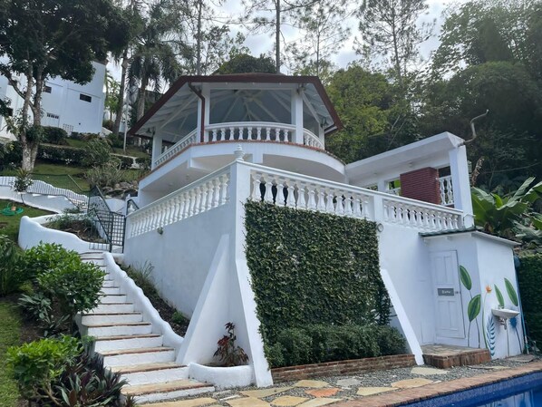 Ein weißes Gebäude mit überdachter Balkon, Treppe und Poolbereich.