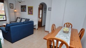 Una sala de estar con un sofá azul, una mesa de comedor con sillas y una lámpara.