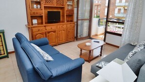 Una sala de estar con un mueble de madera, dos sofás, una mesa de centro y un ventanal corredero que da a un balcón.