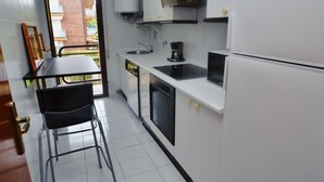 Una cocina compacta con armarios blancos, encimera negra, horno integrado y cafetera.