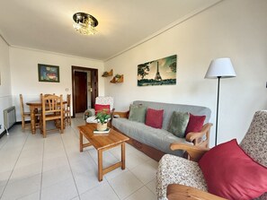 En stue med sofa, lænestole, et sofabord, et spisebord og stole. Der hænger et maleri af Eiffeltårnet på væggen.