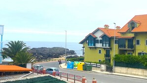 A coastal building with balconies, a road with vehicles, and a view of the sea.