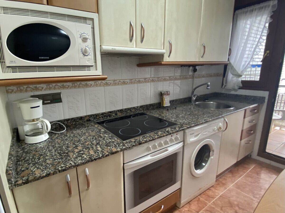 A compact kitchen with a microwave, stove, oven, and washing machine.