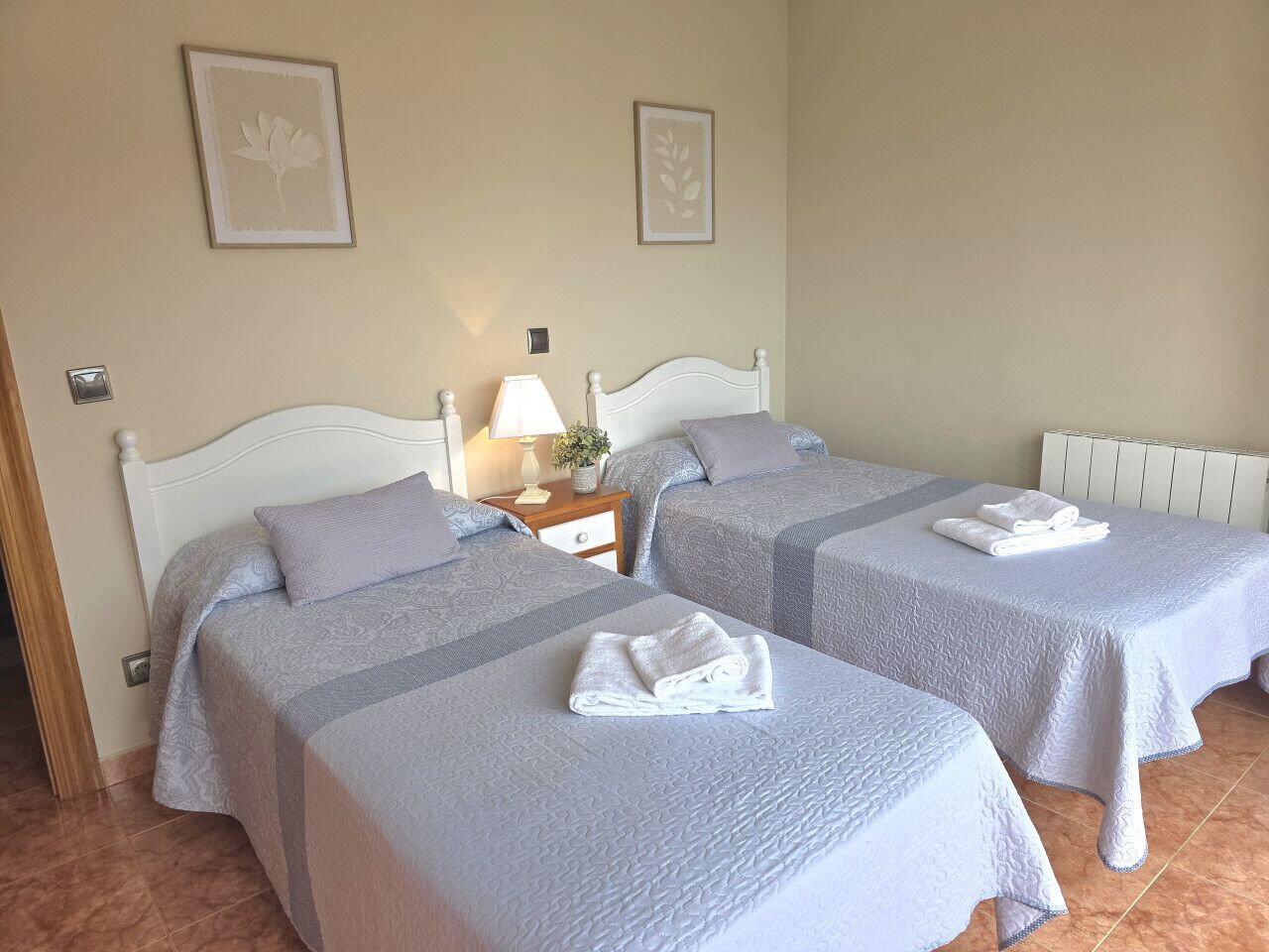 Habitación de hotel con dos camas, una mesita de noche con lámpara y un radiador.