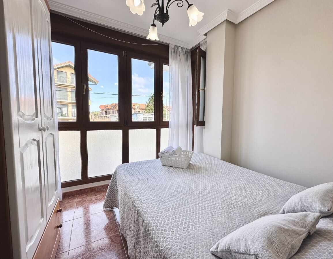 A bedroom with a large window, a bed with a patterned bedspread, and a basket of towels.