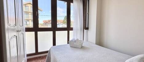 A bedroom with a large window, a bed with a patterned bedspread, and a basket of towels.