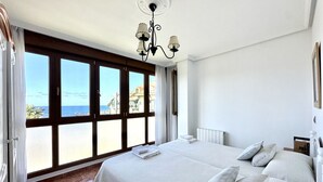 A bedroom with a large bed, a chandelier, a view of the sea, and a window with curtains. - Apartamento con vistas al mar - Pineda 6404 (Noja)