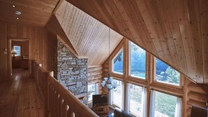 A spacious room with a stone fireplace, large windows, and a wooden staircase.