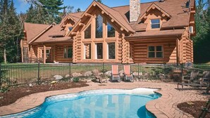 A log cabin with a swimming pool, surrounded by a fence and trees.