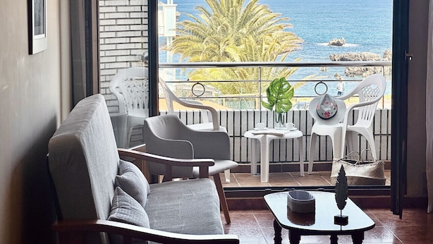 A balcony with a view of the sea, featuring a chair, a small table, and a potted plant.
