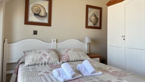 A neatly made bed with patterned bedding and two pillows, a bedside lamp, and two framed shell artworks on the wall.