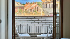 Un balcon avec deux chaises en plastique blanches, un mur de briques et une vue sur des bâtiments en arrière-plan.