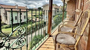 Ein Balkon mit Korbstühlen, Blick auf Nachbarhäuser und einem grünen Metallgeländer.