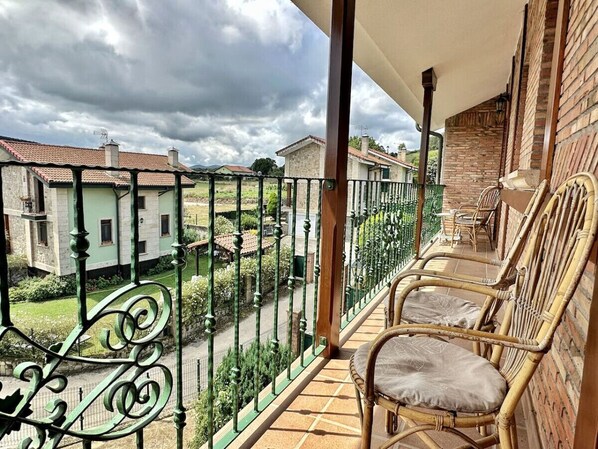 Un balcon avec des fauteuils en osier, une vue sur les maisons voisines et une rambarde en métal vert.