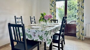 Ein Esszimmer mit Tisch für vier Personen, Stühlen, einer Pendelleuchte und Blick durch ein mit Vorhängen drapiertes Fenster.