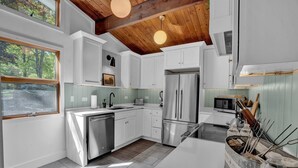 Une cuisine moderne avec des armoires blanches, des appareils en acier inoxydable et un plafond en bois.