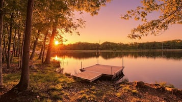 A serene lakeside scene with a wooden dock extending into calm waters, surrounded by trees and a clear sky.