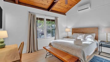 A bedroom with a bed, bedside lamps, a wooden bench, a desk, and a window with curtains.