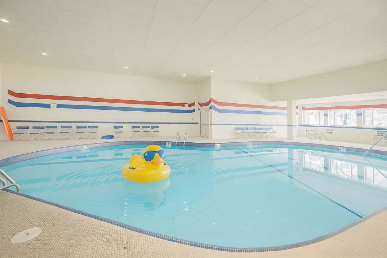 Une piscine intérieure avec un canard jaune gonflable, des murs carrelés et un plafond doté d’un éclairage encastré.