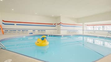Une piscine intérieure avec un canard jaune gonflable, des murs carrelés et un plafond doté d’un éclairage encastré.